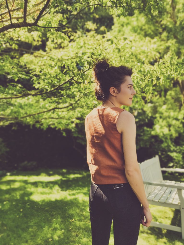 girl architecture student wearing skinny jeans and a brown shirt in lush green leafy garden looking to the side. Sewing Jily Top.