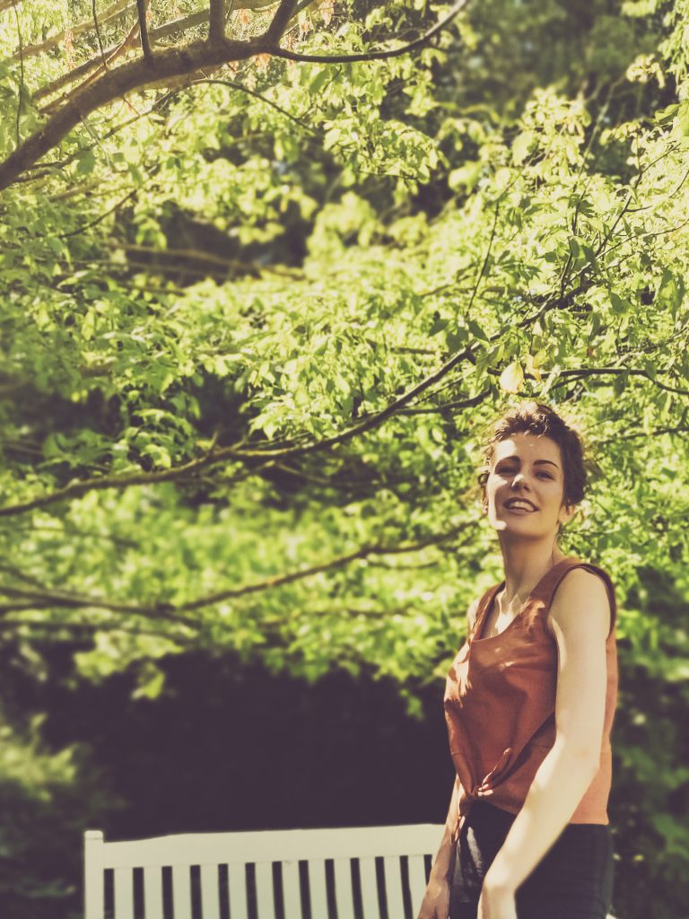 smiling girl architecture student wearing skinny jeans and a brown shirt in lush green leafy garden. sewing Jily Top