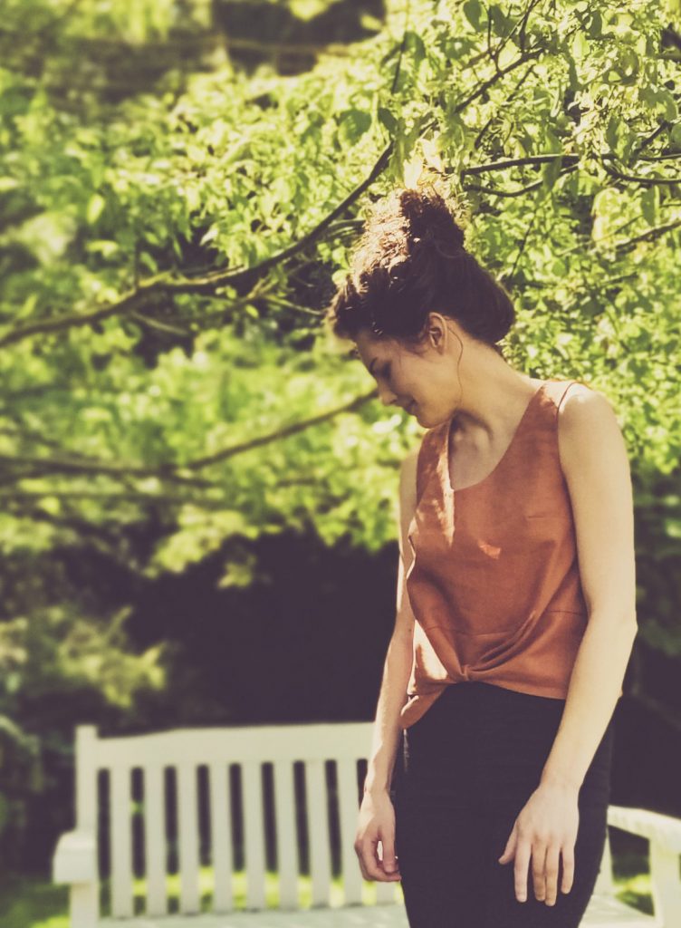 Summer girl with hair in bun wearing black skinny jeans and brown short sleeved Jily Top with a waist tie