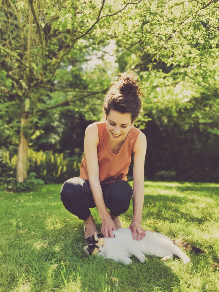 smiling laughing architecture student girl stroking cat wearing handmade brown shirt Jily Top in lush green leafy garden under tree. Sewing Jily Top.