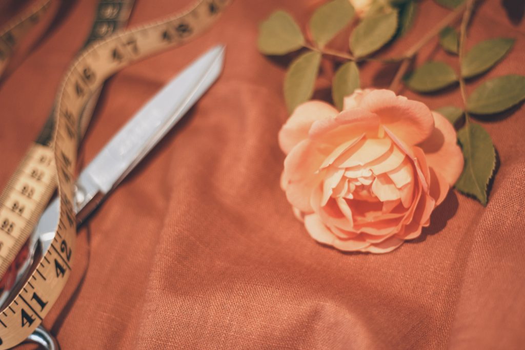 orange rose on orange brown linen with scissors and old fashioned tape measure