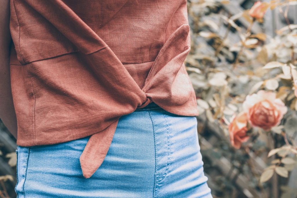 brown linen Jily top with waist tie with blue skinny jeans and roses in background