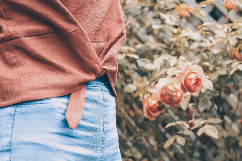 brown linen Jily top with waist tie with blue skinny jeans and roses in background