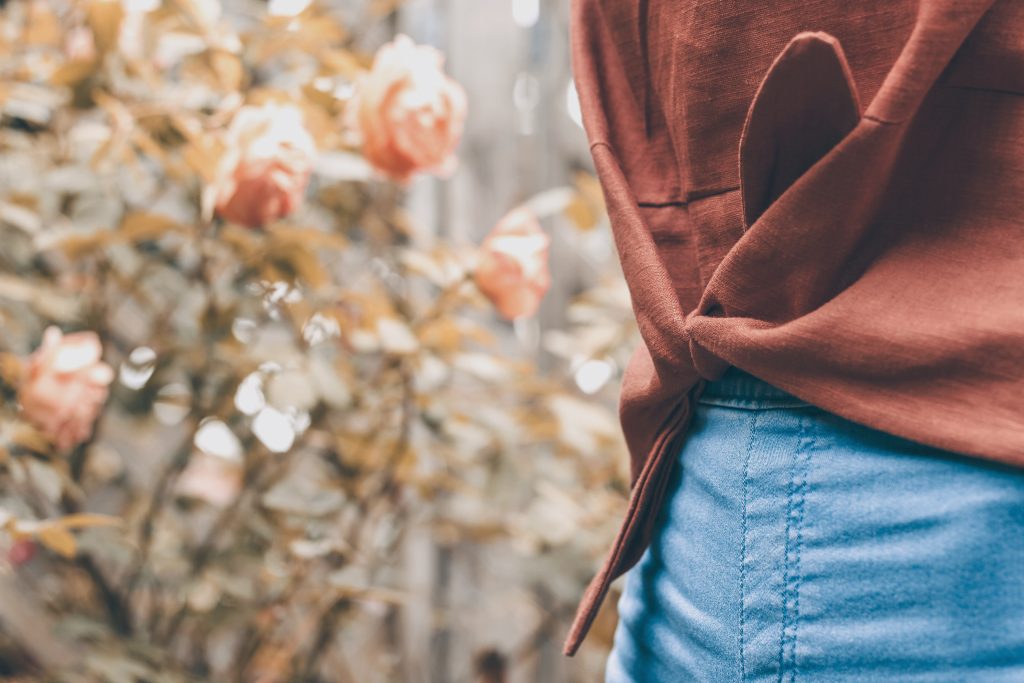 girl wearing blue skinny jeans and brown linen Jily Top waist only wit roses in garden background