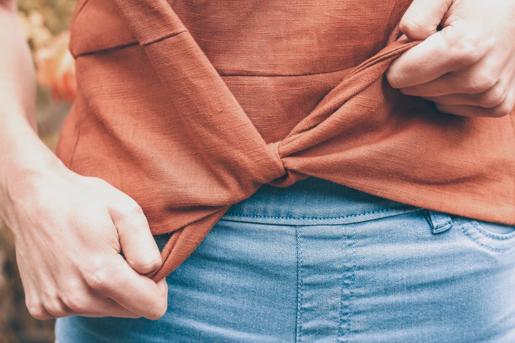 lifestyle girl wearing blue skinny jeans and orange brown linen shirt top tying the waist tie of the shirt